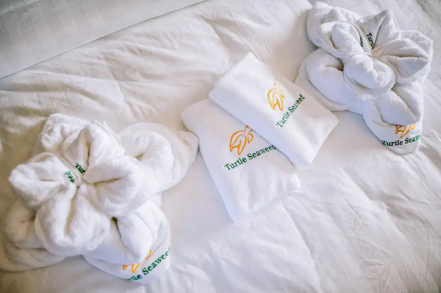 Beautifully folded towel art and custom embroidered towels resting on the bed in the Deluxe Suite at Turtle Seaweed Resort.